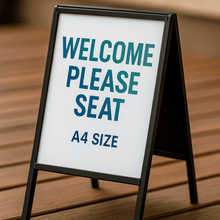 Load image into Gallery viewer, A4 size sign on a wooden surface with text 'WELCOME PLEASE SEAT'.