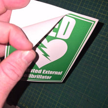 Load image into Gallery viewer, Hand holding a green and white card with an AED symbol on a grid background