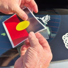 Load image into Gallery viewer, Person holding a car decal with a red and yellow design, applying it to a vehicle's window.