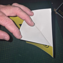 Load image into Gallery viewer, Hand holding a white paper l plate sticker on a green cutting mat