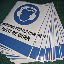 Load image into Gallery viewer, Stack of 'Hearing Protection Must Be Worn' signs on a green cutting mat.
