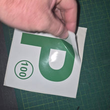 Load image into Gallery viewer, Hand holding a green and white 'P' decal with the number 100 on a green cutting mat.