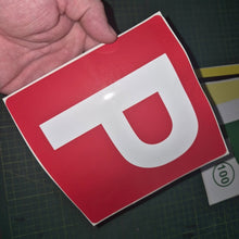 Load image into Gallery viewer, Red square sign with a white 'P' held by a hand on a dark surface.