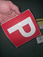 Load image into Gallery viewer, Red square sign with a white 'P' held by a hand on a dark surface.