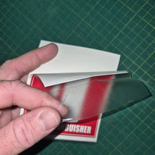 Load image into Gallery viewer, Hand holding a small book or card with a red cover against a green grid background
