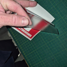 Load image into Gallery viewer, Hand holding a small metallic object on a green cutting mat with a visible brand name.