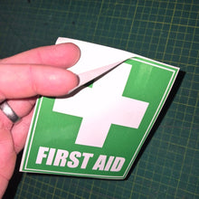 Load image into Gallery viewer, Hand holding a green and white first aid sign on a grid background