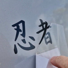 Load image into Gallery viewer, Decal of Japanese font saying ninja characters on a textured surface with a clear plastic sheet.