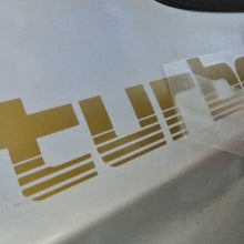 Load image into Gallery viewer, Gold 'Turbo' decal on a white surface
