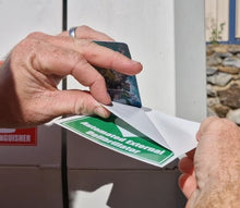 Load image into Gallery viewer, Person holding a green and white label with text, against a neutral background.