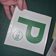 Load image into Gallery viewer, Hand holding a square decal with a green 'P' and number '100' on a green cutting mat.