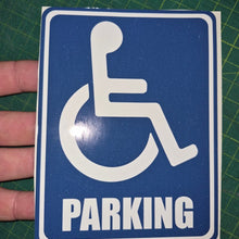 Load image into Gallery viewer, Handicap parking sign held by a hand on a green grid background