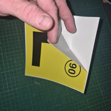 Load image into Gallery viewer, Hand holding a yellow sign with a black letter 'L' and number '90' on a green cutting mat.