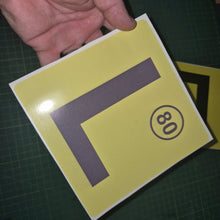 Load image into Gallery viewer, Yellow decal with a large 'L' and number 80 held by a hand on a dark surface.