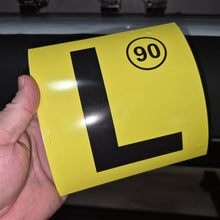 Load image into Gallery viewer, Yellow license plate with black 'L' and number 90 held by a hand against a dark background