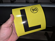 Load image into Gallery viewer, Yellow license plate with black 'L' and number 90 held by a hand against a dark background
