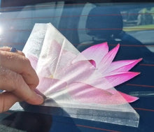 Load image into Gallery viewer, Hand holding a pink flower-shaped car decal against a car window.