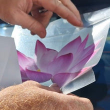 Load image into Gallery viewer, Person peeling back a car window film with a pink flower design.