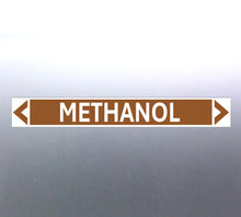 Load image into Gallery viewer, A pipe marker label with the word 'METHANOL' in bold black lettering on a golden tan background, with a white border and green directional arrows pointing in both directions.