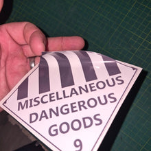 Load image into Gallery viewer, Hand holding a triangular label with 'Miscellaneous Dangerous Goods' text on a green cutting mat.