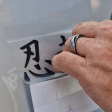 Load image into Gallery viewer, Hand with a ring holding a transparent sheet with black characters against a light background