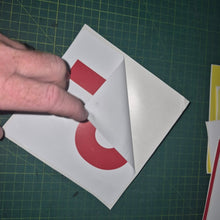 Load image into Gallery viewer, Hand folding a piece of vinyl sticker with a red circle on a green cutting mat.