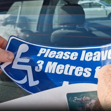 Load image into Gallery viewer, Hand holding a blue and white decal with a wheelchair icon and text 'Please leave 3 Metres' in front of a car.