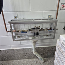 Load image into Gallery viewer, Plumbers cage attached to a wall with pipes and a stack of newspapers on the ground.
