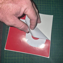 Load image into Gallery viewer, Hand peeling a white sticker from a red and white square on a green cutting mat.