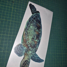 Load image into Gallery viewer, Sticker of a turtle on a piece of paper held by a hand on a green cutting mat.