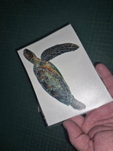 Load image into Gallery viewer, Hand holding a card with a turtle illustration on a dark grid background