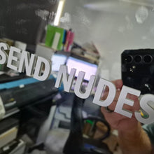 Load image into Gallery viewer, Person holding a phone with 'SEND NUDES' text in a room with equipment and supplies.