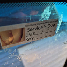 Load image into Gallery viewer, Service due date label on a car windshield with water droplets.