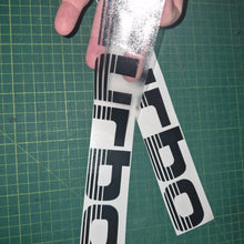 Load image into Gallery viewer, Two 'Turbo' decals being held over a green cutting mat.