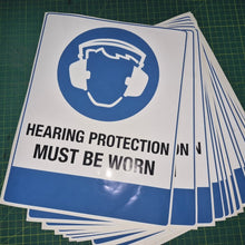 Load image into Gallery viewer, Stack of 'Hearing Protection Must Be Worn' signs on a green grid background