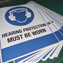 Load image into Gallery viewer, Stack of 'Hearing Protection Must Be Worn' signs on a green cutting mat.