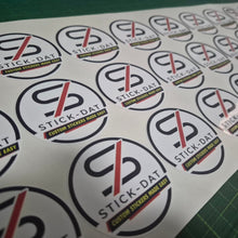 Load image into Gallery viewer, Sheet of Stick-Dat stickers with brand logo on a cutting mat.