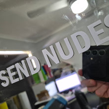 Load image into Gallery viewer, Sticker Text 'SEND NUDES' overlaid on a blurred indoor setting with electronic devices.