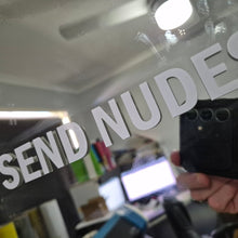 Load image into Gallery viewer, Sticker Text 'SEND NUDES' overlaid on a blurred indoor setting with electronic devices.