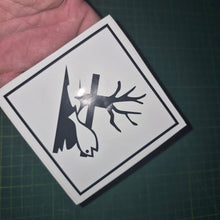 Load image into Gallery viewer, Sticker with a black silhouette of a tree and fish on a white background, held over a dark surface.