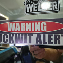 Load image into Gallery viewer, Sticker with 'WARNING FUCKWIT ALERT' text held by a person, with a blurred background.