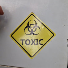 Load image into Gallery viewer, Toxic warning sign on a metallic surface with a hand partially visible.