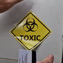 Load image into Gallery viewer, Yellow 'TOXIC' sign with biohazard symbol on a metallic surface.