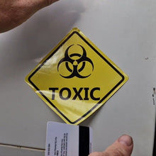 Load image into Gallery viewer, Yellow 'TOXIC' sign with biohazard symbol on a metallic surface.