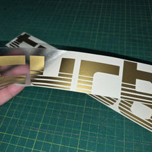 Load image into Gallery viewer, Gold and brown decal held over a larger decal on a green cutting mat.