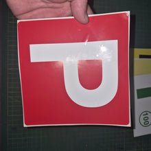 Load image into Gallery viewer, Red square sign with a white 'P' held by a hand on a dark background