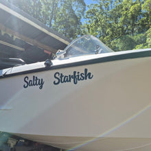 Load image into Gallery viewer, Boat named 'Salty Starfish' with a blurred background of trees and a building.