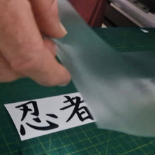 Load image into Gallery viewer, Hand holding a piece of translucent material over a sheet with Japanese characters on a green cutting mat.