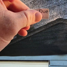 Load image into Gallery viewer, Hand holding a small rectangular card with 'rego Due' sticker against a smooth window surface.