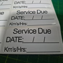 Load image into Gallery viewer, Service due label with fields for date, kilometers, and hours on a green cutting mat.
